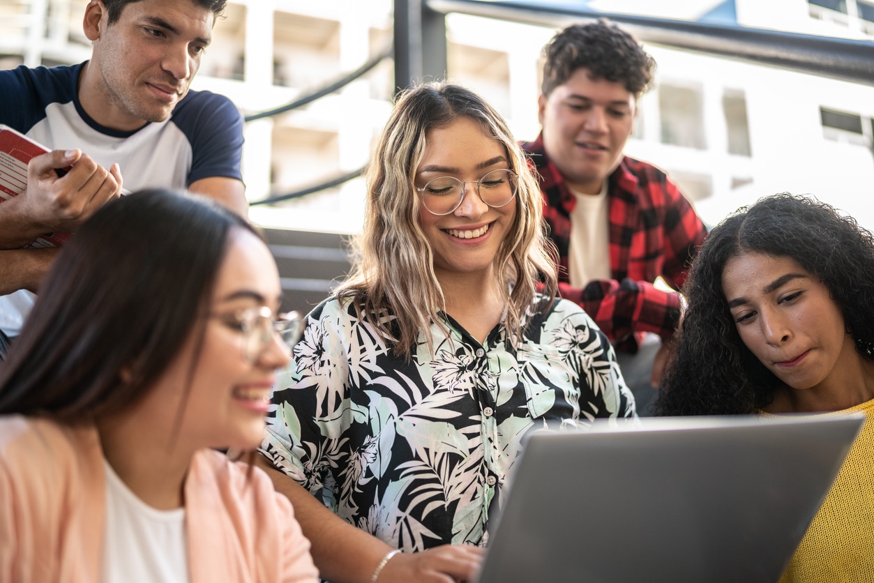 Young woman showing something on the laptop to her friends on university stairs